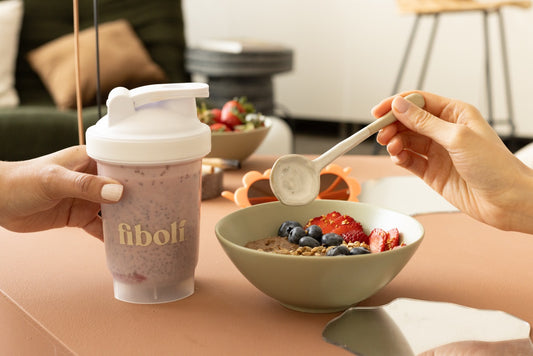 Person holding a fiboli shaker cup next to a bowl of Chocolaah Fiboli with fruit.
