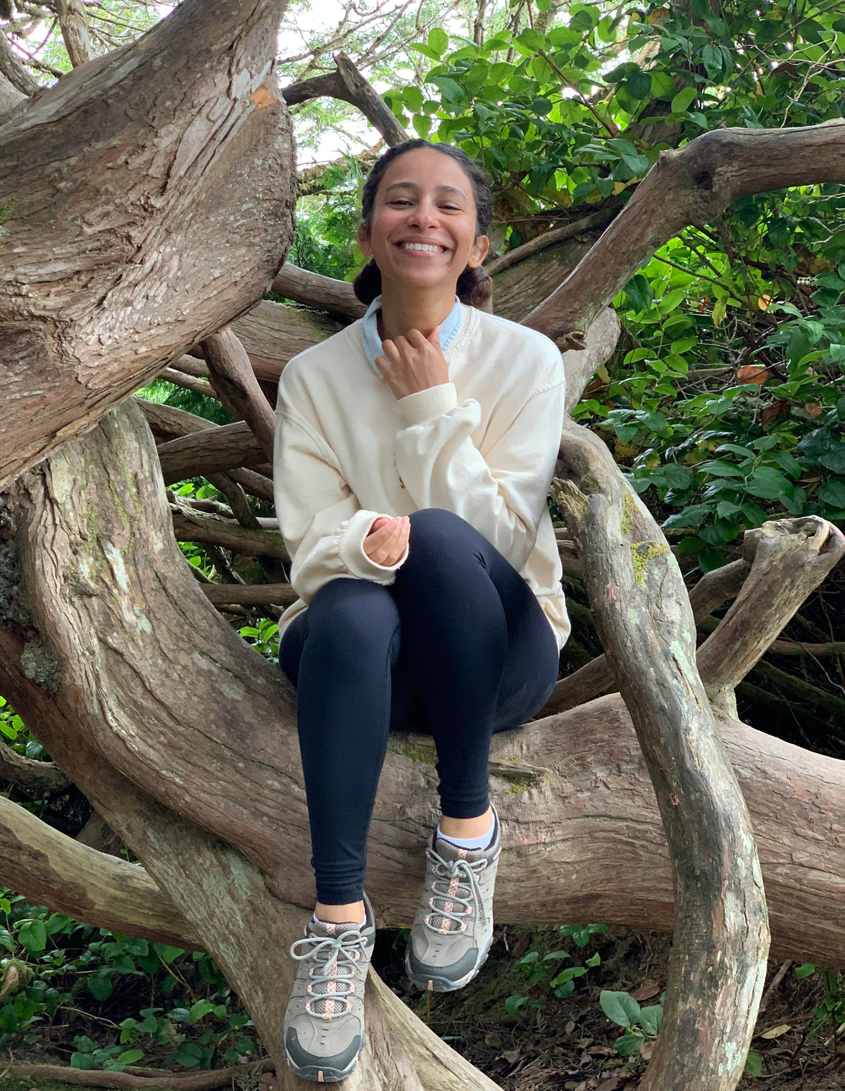 Person sitting on a large tree branch in a natural setting is Rania, the founder of fiboli, she is smiling. 